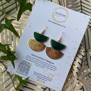 Op de afbeelding: Gouden en groene geometrische oorbellen op een witte kaart met de tekst "AURORE design" en "www.designmyaurore.eu". De kaart bevat ook de tekst "Handgemaakt in België" en "Geniet!" met een QR-code en social media-iconen.