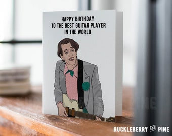 Pode incluir: Um cartão branco com o texto "HAPPY BIRTHDAY TO THE BEST GUITAR PLAYER IN THE WORLD." O cartão apresenta uma ilustração de um homem segurando uma guitarra. O homem está usando um terno cinza, uma camisa rosa e uma gravata borboleta verde.