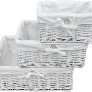 May include: Three white wicker baskets with white fabric liners. The baskets are stacked on top of each other, with the largest basket at the bottom and the smallest basket at the top. The baskets have a woven design and are ideal for storage.