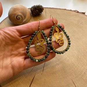 Könnte beinhalten: Ein Paar goldene Schlangenohrringe mit grünen Edelsteinperlen. Die Schlange ist ein Ausschnittdesign und die Perlen sind rund.