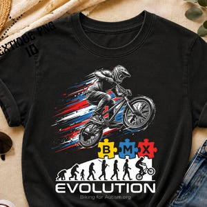 May include: Black t-shirt featuring a BMX rider in action with red, white, and blue streaks. The design includes the word "EVOLUTION" with a progression of figures and puzzle pieces. The text "Biking for Autism.org" is also present.