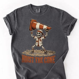 May include: Dark grey t-shirt featuring a baseball-themed skeleton character holding a traffic cone. The skeleton wears a baseball uniform and a headband. The text "HOIST THE CONE" is printed below the character.