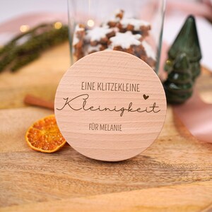 Könnte beinhalten: Ein rundes Holzschild mit dem Text "Eine klitzekleine Kleinigkeit für Melanie" und einem kleinen Herzsymbol.