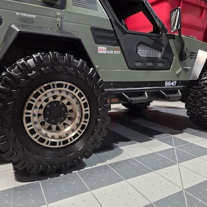 May include: A detailed image of a green and black model off-road vehicle with large, rugged tires. The tires have a diameter of approximately 5 inches. The vehicle features a detailed chassis and a roll cage, suggesting a hobbyist or collector's item.