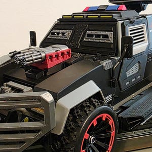 May include: Black toy armored vehicle with red and gray accents. Features a gun turret, large tires with red rims, and a step. The vehicle has a rugged design and is likely a toy.