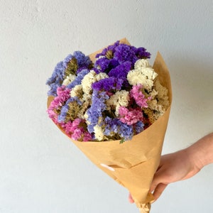 May include: A bouquet of dried flowers in shades of purple, pink, and white, wrapped in brown paper.
