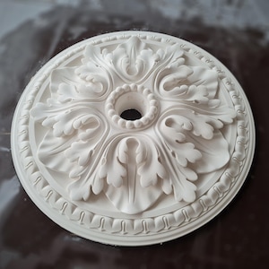 May include: White plaster ceiling medallion with a decorative floral design. The medallion has a central hole for a light fixture.