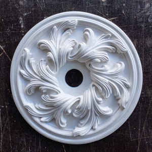 May include: White plaster ceiling medallion with a decorative floral design. The medallion has a circular shape and a central hole.