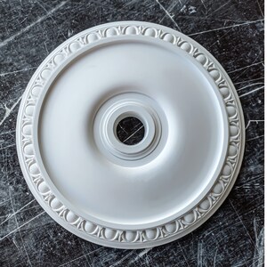 May include: White ceiling medallion with a decorative border and a central hole. The medallion is made of a lightweight material and is designed to be used as a decorative element in a ceiling.
