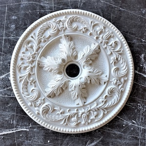 May include: White ceiling medallion with a decorative floral design. The center of the medallion features a five-pointed star with a circular opening in the middle.