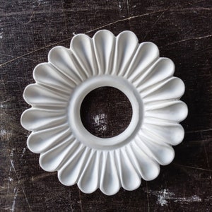 May include: White plaster ceiling medallion with a circular cutout in the center and a decorative flower design around the edge.