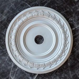 May include: White ceiling medallion with a decorative, ornate design. The medallion has a circular shape with a smaller circle in the center.