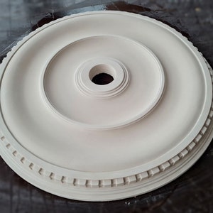 May include: White ceiling medallion with a decorative border and a center hole. The medallion is made of a lightweight material and is designed to be used as a decorative element in a ceiling.