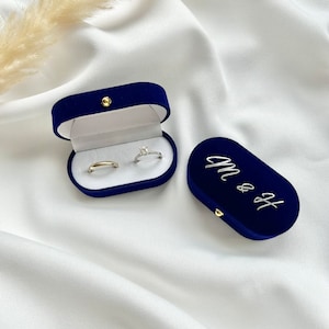 Könnte beinhalten: Zwei Samt-Ringboxen, eine blaue mit der Aufschrift "Mr & Mrs" und die andere blaue mit zwei goldenen Ringen darin.