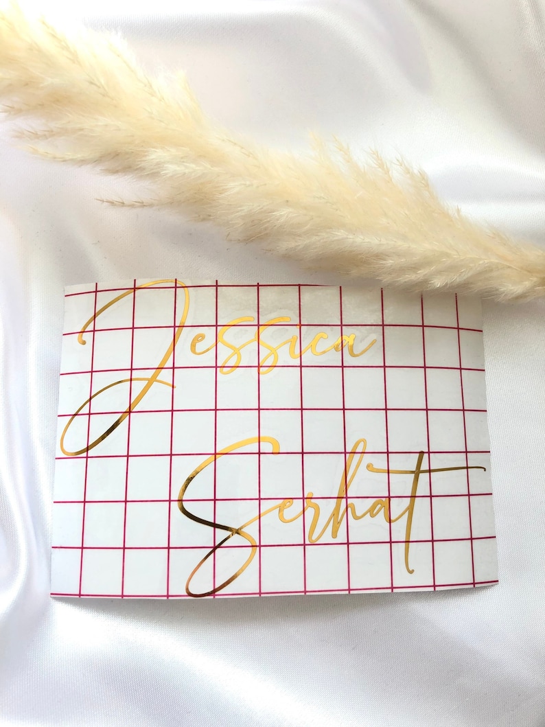 May include: Gold vinyl lettering on a white background with a red grid pattern. The lettering reads "Jessica Serhat".