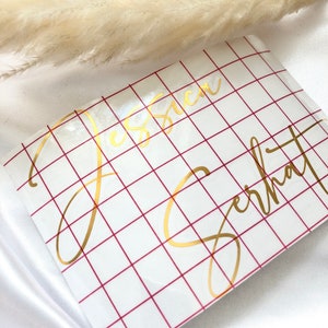 May include: A white sheet of paper with a red grid pattern. The names "Jessica" and "Gerhardt" are written in gold cursive lettering on the paper.