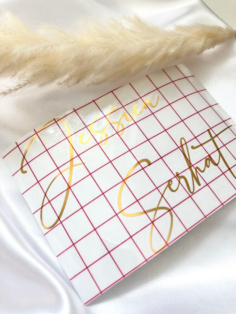 May include: A white sheet of paper with a red grid pattern. The names "Jessica" and "Gerhardt" are written in gold cursive lettering on the paper.