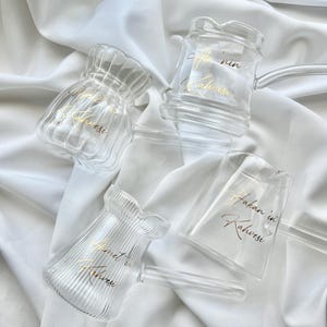 Op de afbeelding: Vier Turkse koffiekannen van helder glas met gouden belettering. De belettering luidt "Hakan'in Kahvesi", "Ahmet'in Kahvesi", "Ali'nin Kahvesi" en "Ayse'nin Kahvesi".