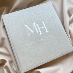 Op de afbeelding: Een grijs linnen fotoalbum met de initialen "M H" en de tekst "Melis & Hasan Cem" in wit gedrukt.