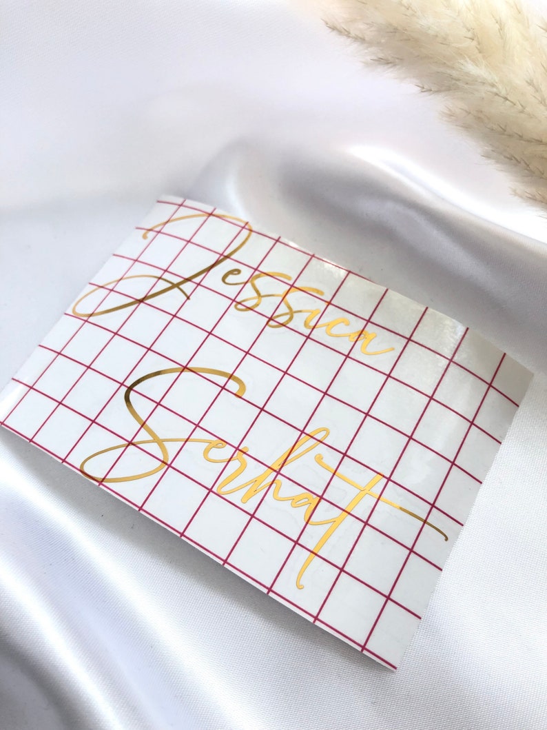 May include: A white sheet of paper with a red grid pattern. The names "Jessica" and "Schmat" are written in gold cursive lettering on the paper.