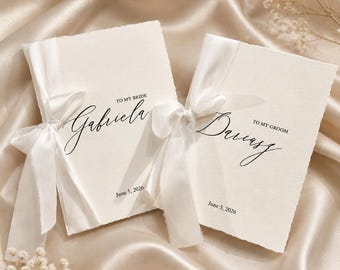 Könnte beinhalten: Zwei elfenbeinfarbene Hochzeitskarten mit weißen Satinbändern auf einer Satin-Oberfläche. Auf der linken Karte steht "To My Bride Gabriela June 5, 2026." Auf der rechten Karte steht "To My Groom Dariusz June 5, 2026."