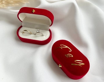 May include: Two red velvet ring boxes. One box is open and contains two gold rings, one with a diamond. The other box is closed and has the words "To & From" written in gold lettering.