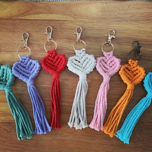 Puede incluir: Siete llaveros de macramé en forma de corazón de colores con borlas. Los llaveros están hechos con hilo de diferentes colores y presentan una forma de corazón con un diseño anudado.