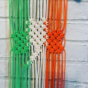 Pode incluir: Uma tape&ccedil;aria de macram&eacute; verde, branca e laranja com uma etiqueta "Handmade with love" anexada.
