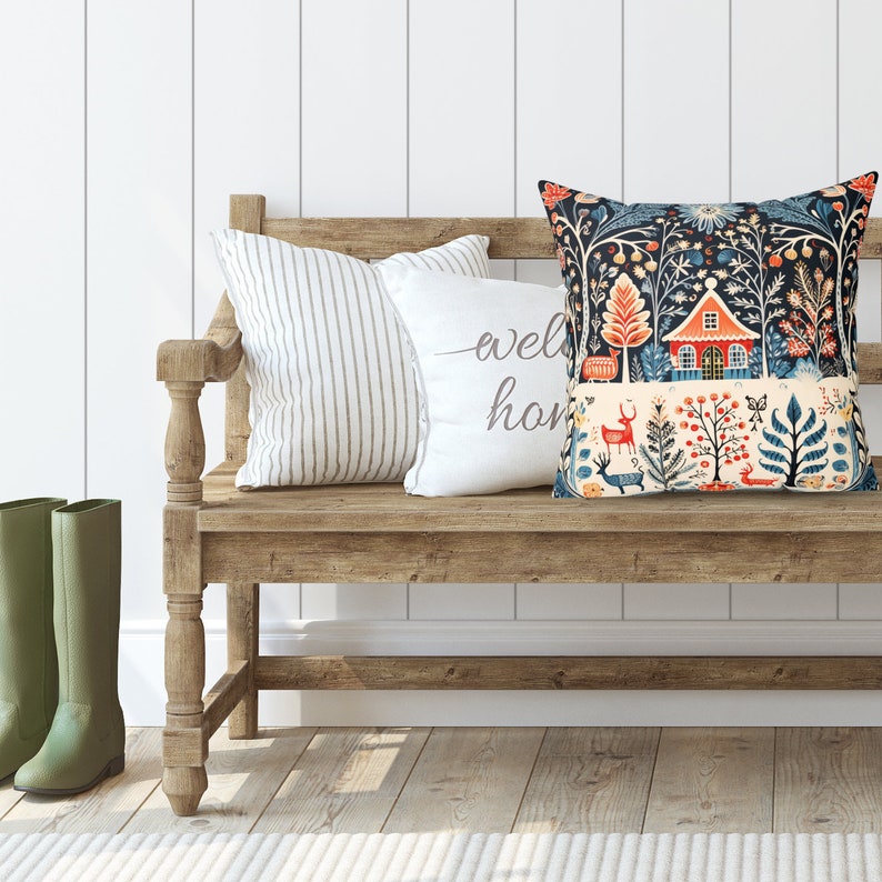 May include: A cushion with a forest scene design, including a red house, deer, and floral patterns. It sits on a wooden bench alongside two other cushions, one striped and one with the words "welcome home". Green wellington boots are visible.
