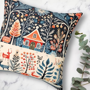 May include: Square cushion with a forest-themed design. The cushion has a navy blue backdrop with a cream-coloured band. The illustration includes a red house, deer, trees, and floral motifs in orange, blue, and cream hues. The cushion is square.