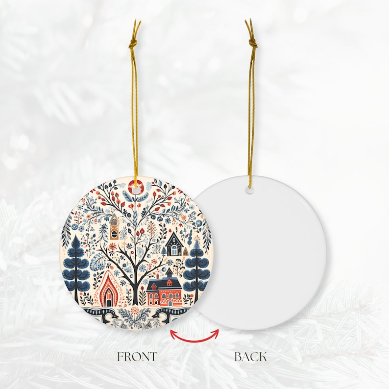 May include: A round ceramic Christmas ornament with a folk art design. The front features a tree with houses, flowers, and other details in red, blue, and beige. The back is plain white. A gold string is attached for hanging.