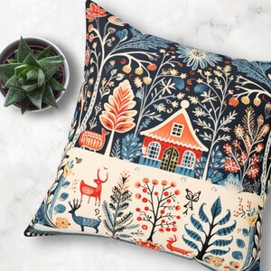 May include: Square cushion with a forest-themed design. The navy blue background is adorned with a cream-coloured band. The illustration includes a red house, deer, trees, and floral motifs in orange, blue, and cream. The cushion is square-shaped.