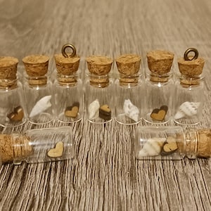 May include: Clear glass bottles with cork stoppers, each containing small decorative elements. Some bottles hold wooden hearts, others contain seashells. The bottles are arranged on a wooden surface.