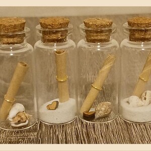 May include: Six small glass bottles with cork tops, each containing a rolled up piece of paper, sand, and small decorative items. The bottles are arranged in a row on a wooden surface.