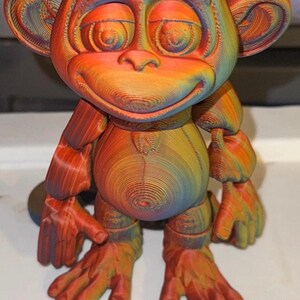 Op de afbeelding: Een 3D-geprinte apenfiguur in regenboogkleuren. De aap heeft een lachend gezicht, grote oren en beweeglijke ledematen. Het cijfer "2" staat in het zwart onderaan. Geschikt voor woondecoratie.