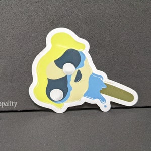 May include: A yellow and blue melting popsicle with a stick. The popsicle is melting and dripping blue liquid.