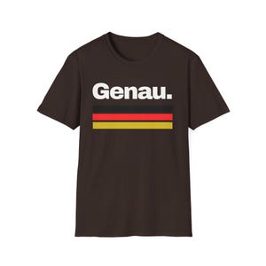 May include: A dark brown t-shirt with the word "Genau." printed in white letters. The shirt features a horizontal stripe design in the colors of the German flag: black, red, and gold.