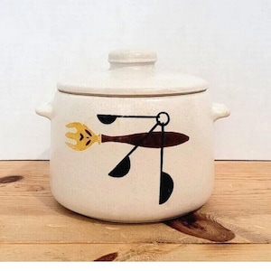 May include: White ceramic crock pot with a lid. The crock pot has a brown and black design of a wooden spoon, fork, and measuring spoons.