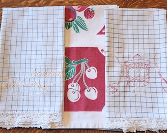 Könnte beinhalten: Eine Sammlung von Vintage-Küchenwäsche. Zwei blau-weiß karierte Handtücher mit Spitzenbesatz und gestickten Details. Ein rot-weißes Küchentuch mit Kirschmotiv ist ebenfalls enthalten.