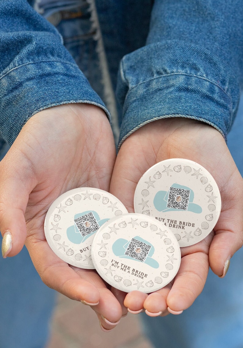 May include: Three round white paper coasters with a blue and white design. Each coaster features a QR code, a seashell border, and the text "Buy the Bride a Drink" or "I'm the Bride Buy Me a Drink".