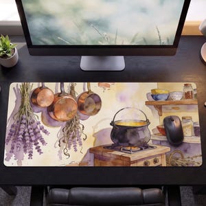 May include: A rectangular desk mat featuring a watercolor illustration of a kitchen scene with hanging copper pots, bundles of lavender, and a black cauldron simmering on a stove. The artwork includes shelves with jars and bowls, rendered in soft tones.