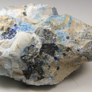 May include: A rough, gray rock with blue and white mineral deposits. The rock has a dark gray, almost black, mineral vein running through it.