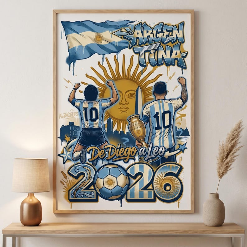 May include: A framed poster featuring two football players in light blue and white striped jerseys with the number 10, the Argentine flag, a golden sun emblem, a trophy, a football, and the text "ARGENTINA" and "De Diego a Leo 2026".