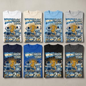 May include: Eight t-shirts in various colours featuring a graphic print of the Argentina flag, a sun, a football player with the number 10, a trophy, and the text "ARGENTINA" and "De Diego a Leo 2026" displayed in a stylised blue and gold font.