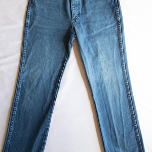 Puede incluir: Un par de pantalones vaqueros de mezclilla en tono azul medio con un dise&ntilde;o cl&aacute;sico de cinco bolsillos, cierre de botones y remaches de color cobre en las esquinas de los bolsillos. Corte recto con costuras visibles en los laterales.
