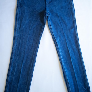 May include: A pair of high-waisted blue denim jeans featuring a classic five-pocket design, a front zip fly with a button fastening, and copper-toned rivets at the pocket corners. The legs are straight-cut with a slightly frayed hem at the bottom.