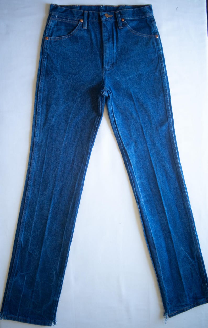 May include: A pair of high-waisted blue denim jeans featuring a classic five-pocket design, a front zip fly with a button fastening, and copper-toned rivets at the pocket corners. The legs are straight-cut with a slightly frayed hem at the bottom.
