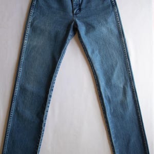 May include: A pair of high-waisted blue denim jeans featuring a classic five-pocket design, a front zip fly with a button fastening, and visible copper-toned rivets at the pocket corners. The fabric has a medium wash with subtle fading.