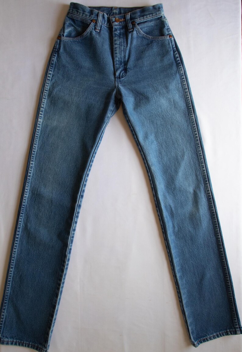 May include: A pair of high-waisted blue denim jeans featuring a classic five-pocket design, a front zip fly with a button fastening, and visible copper-toned rivets at the pocket corners. The fabric has a medium wash with subtle fading.