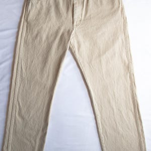 Op de afbeelding: Een beige spijkerbroek met een klassiek ontwerp met vijf zakken, een knoopsluiting en koperkleurige metalen klinknagels op de hoeken van de zakken. De broek heeft een recht model met zichtbare stiksels langs de zijnaden en de tailleband.